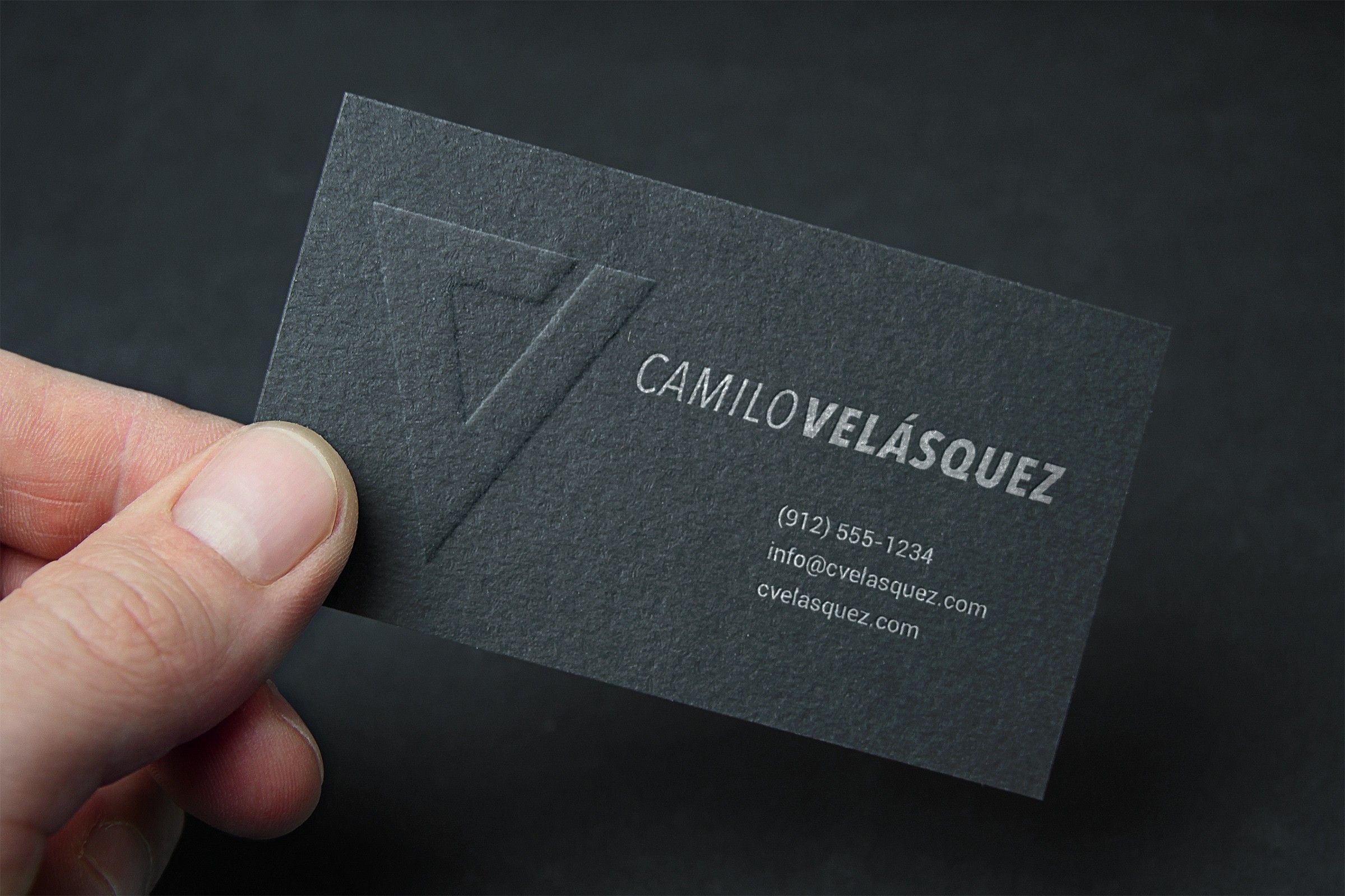 Hand holding a dark grey business card with the V monogram embossed