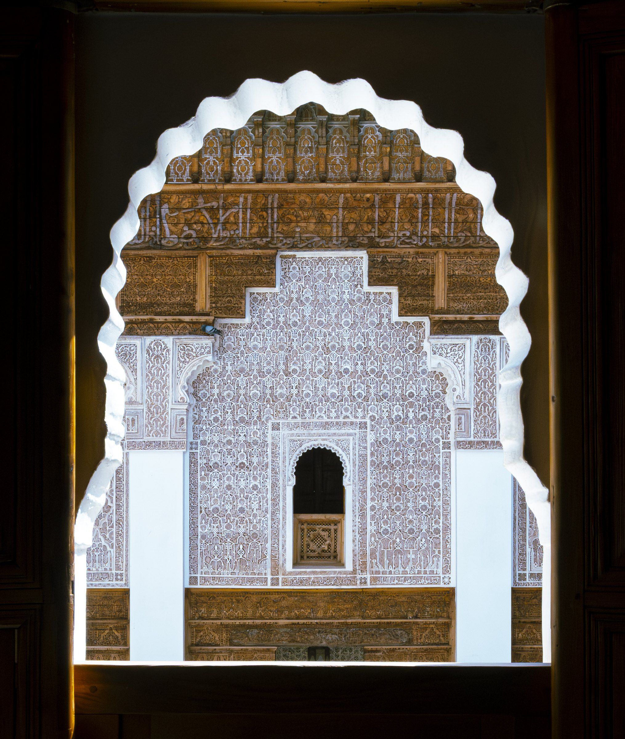 Intricately carved stucco and cedar wall of a courtyard, seen through a scalloped arch window