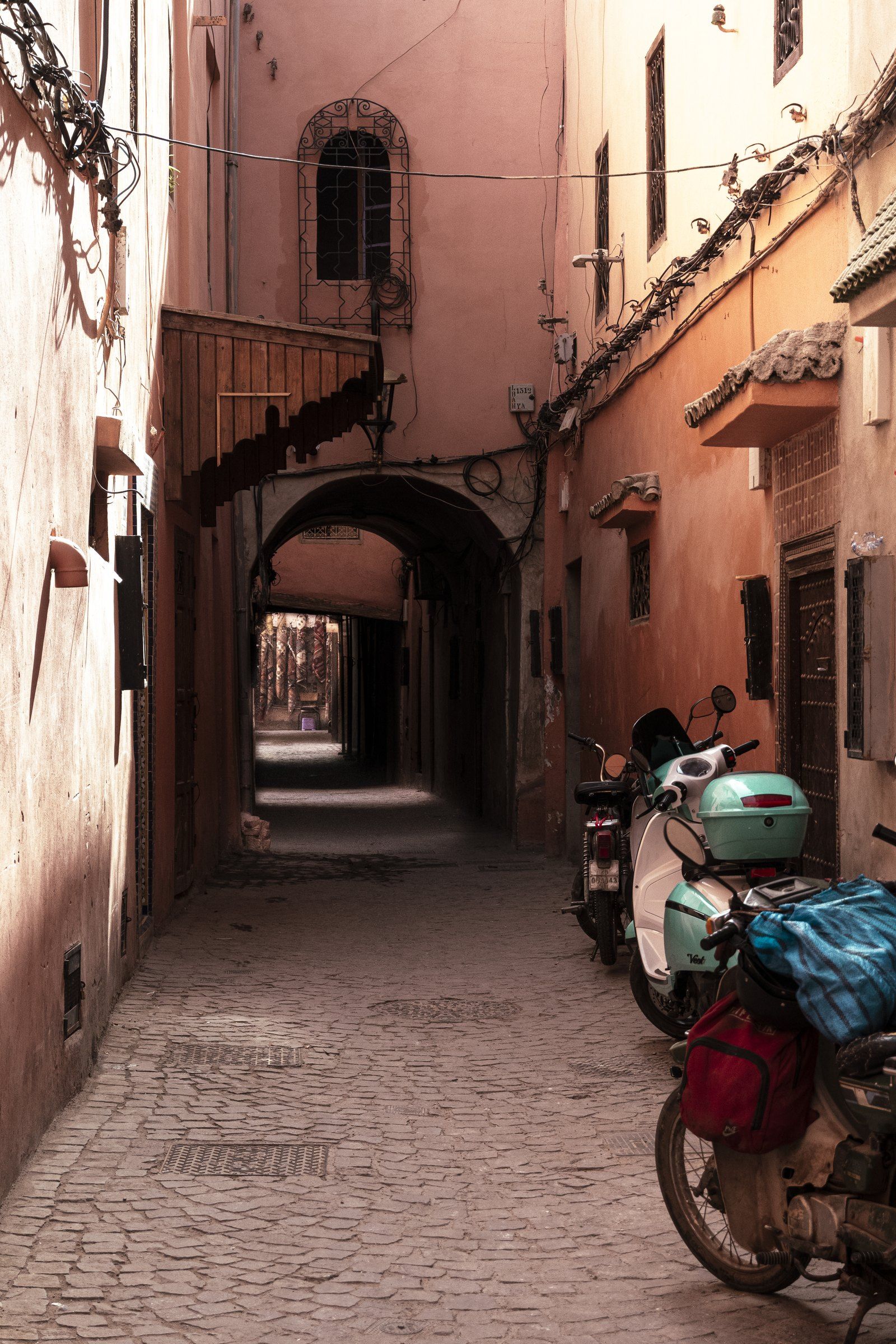 Narrow pink-walled alley with motorbikes parked beside an arched passage