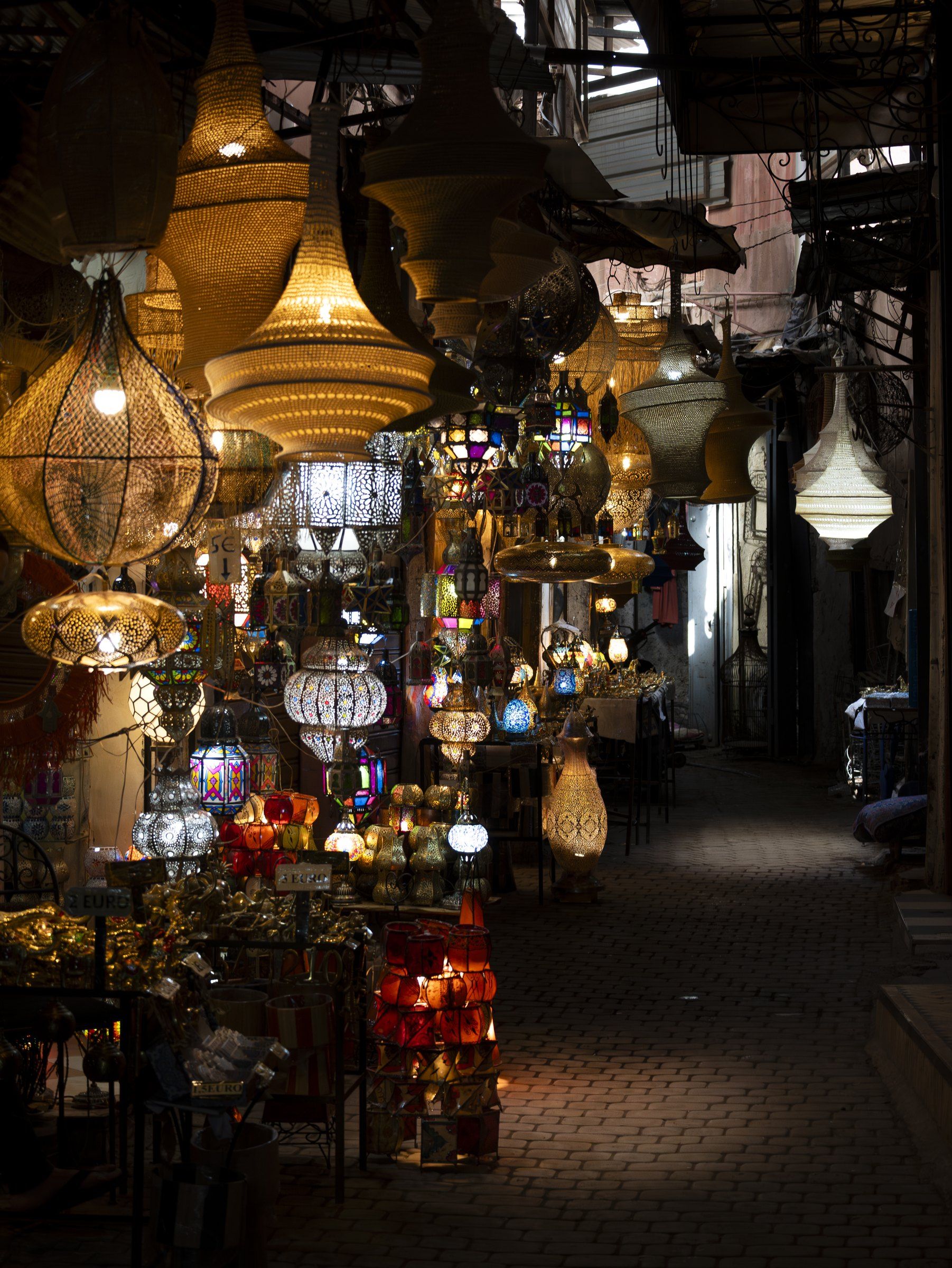 A lantern shop spilling into a dim alley, dozens of lamps glowing gold