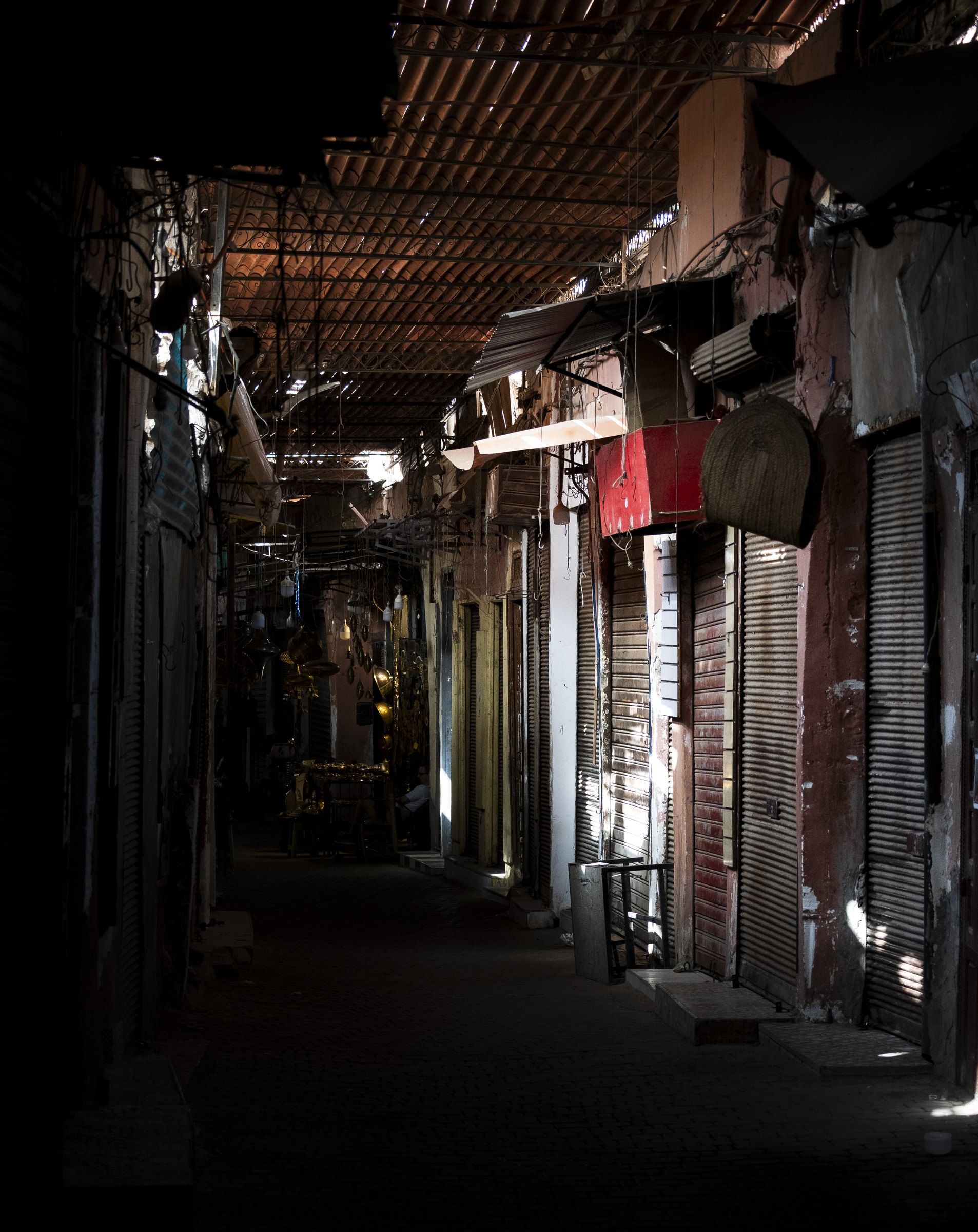Covered souk alley with closed shutters and slatted light falling across the walls
