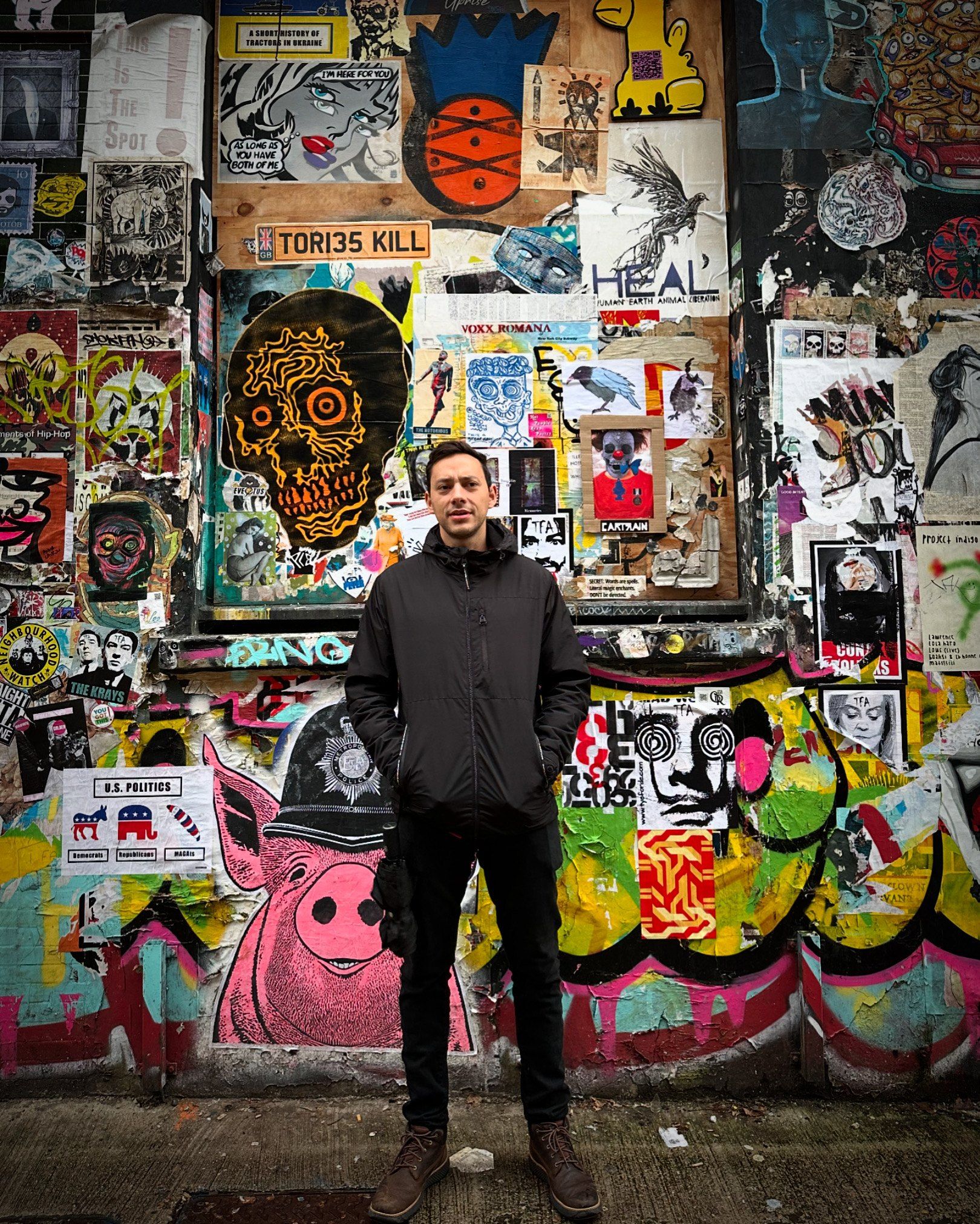 Juan Posada standing in front of a wall covered in colourful street art and posters